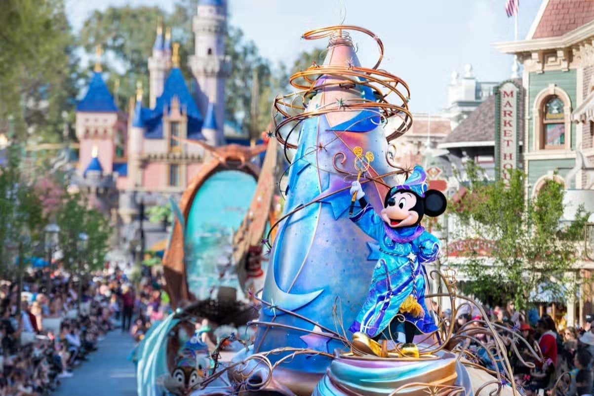 A parade with Mickey Mouse at the forefront travelling down the main street of Disneyland