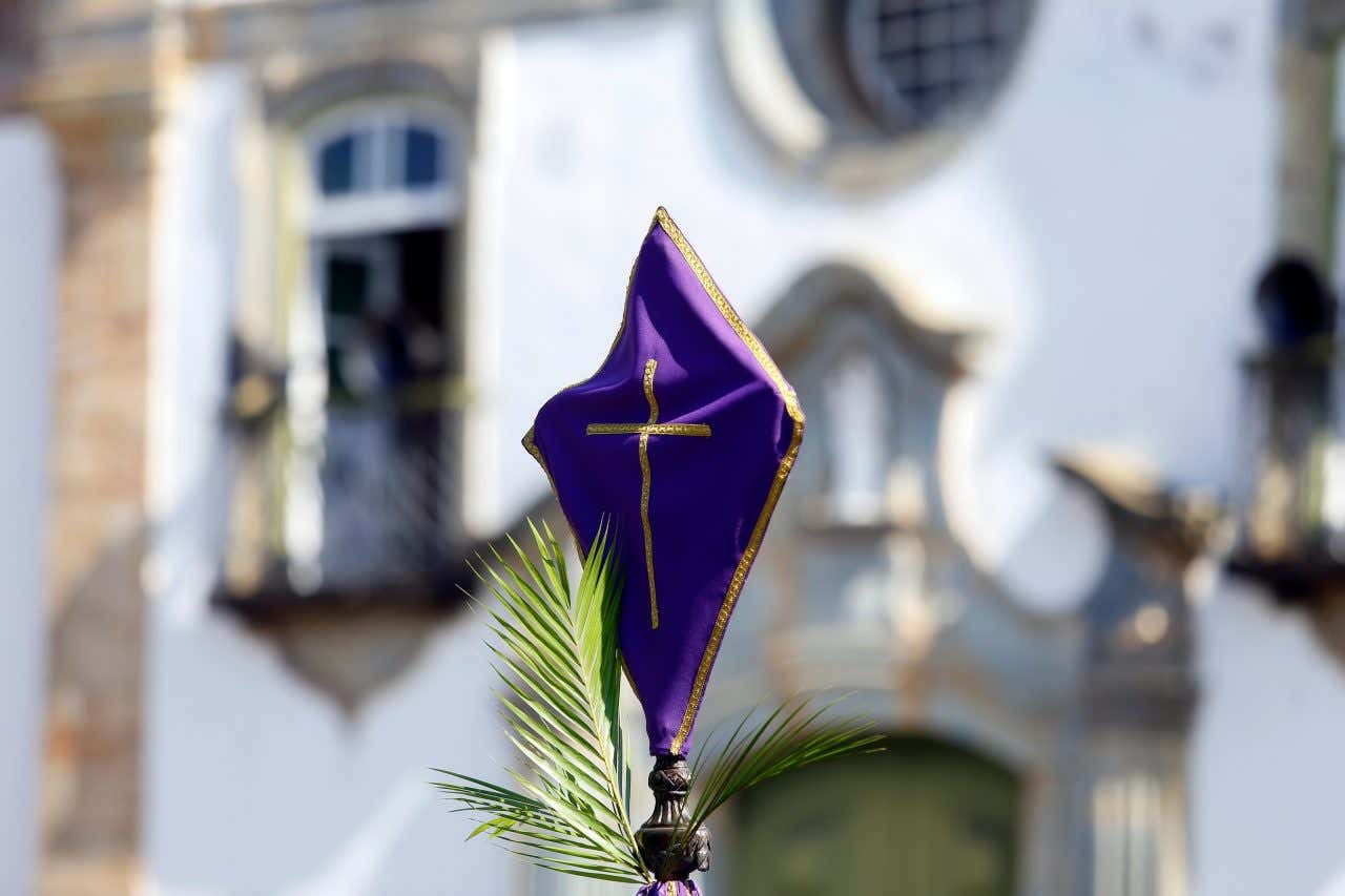 Cruz coberta com tecido roxo durante a procissão da Semana Santa com uma igreja ao fundo