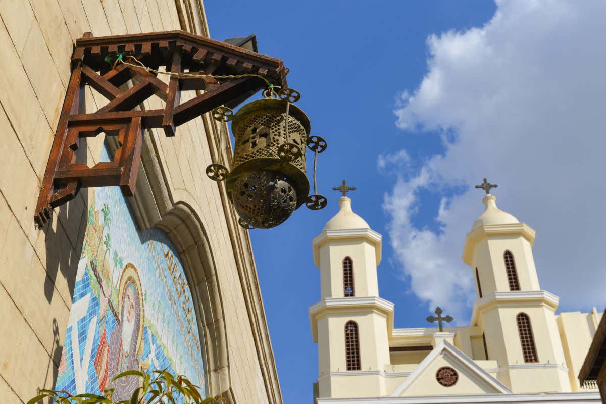 A church with a white facade and two towers on a Cairo street decorated with a religious mosaic and a lantern.