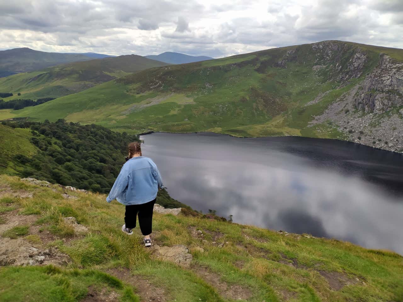 Clara Aragón de espaldas con el lago Guinness de fondo, vegetación y varias nubes grises en el cielo