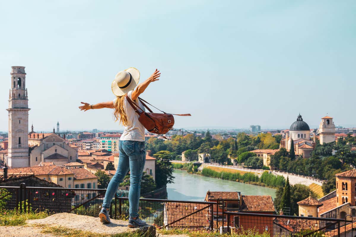 Una turista de espaldas a la cámara y con los brazos extendidos contemplando el río de Verona y varias iglesias