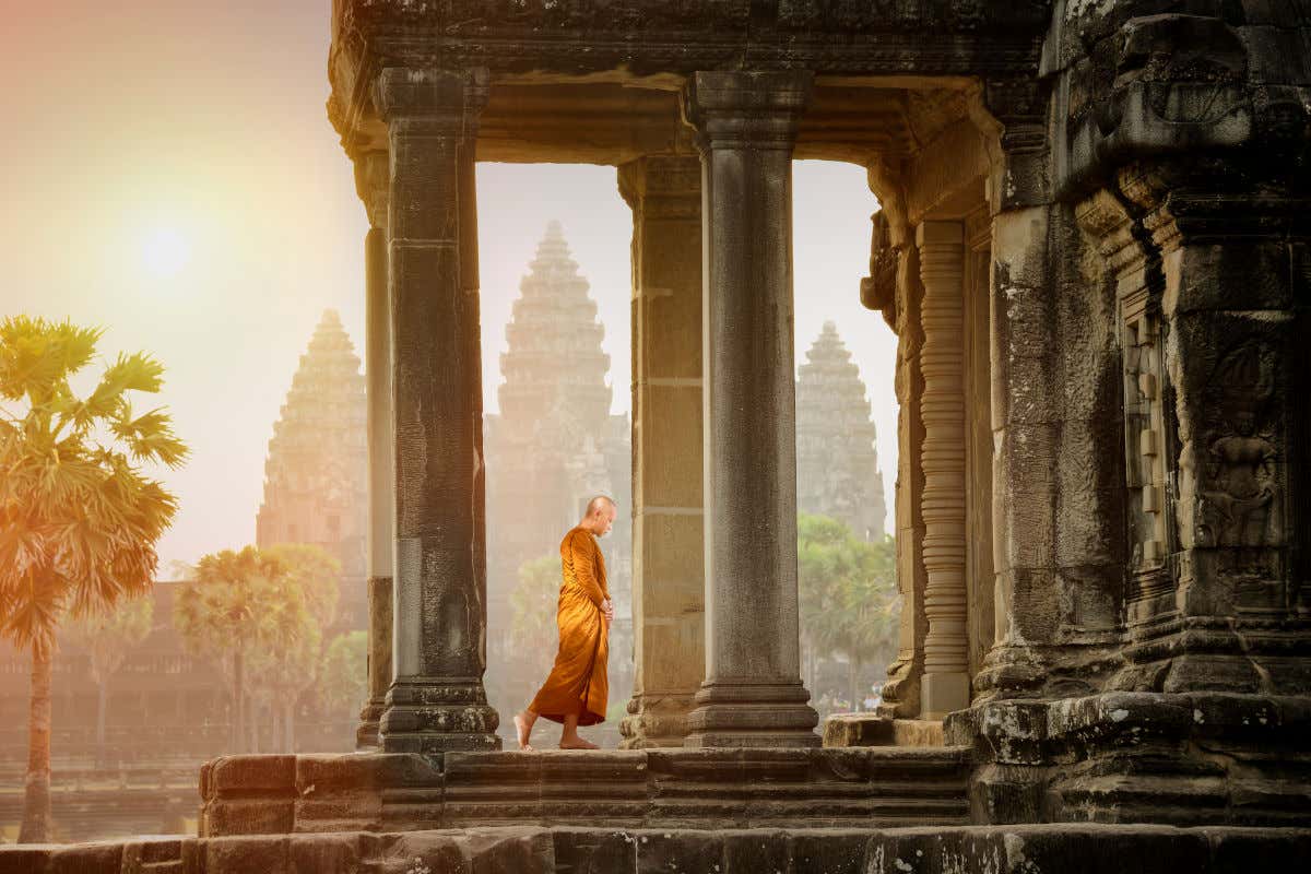 Un monje budista con una túnica naranja entre las altas columnas de uno de los templos de Angkor