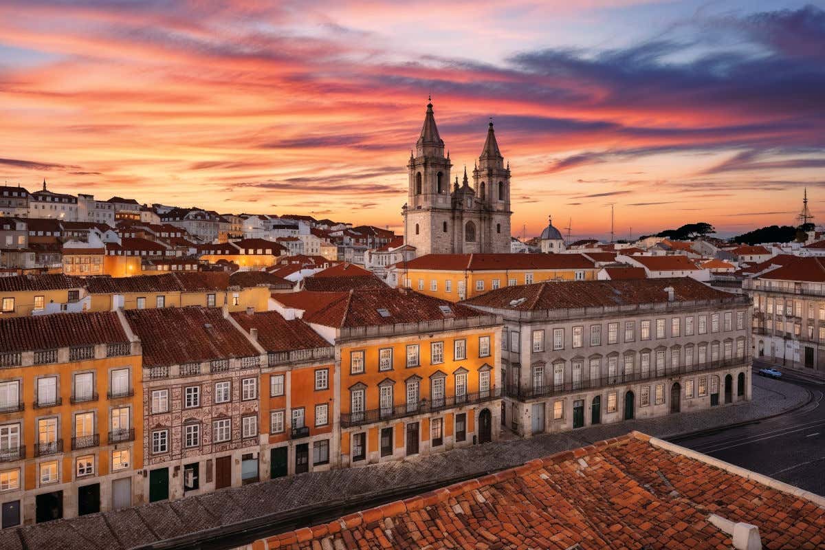 Vista aérea del centro histórico de Lisboa con varias casas de colores con tejas y una catedral con dos torres al atardecer