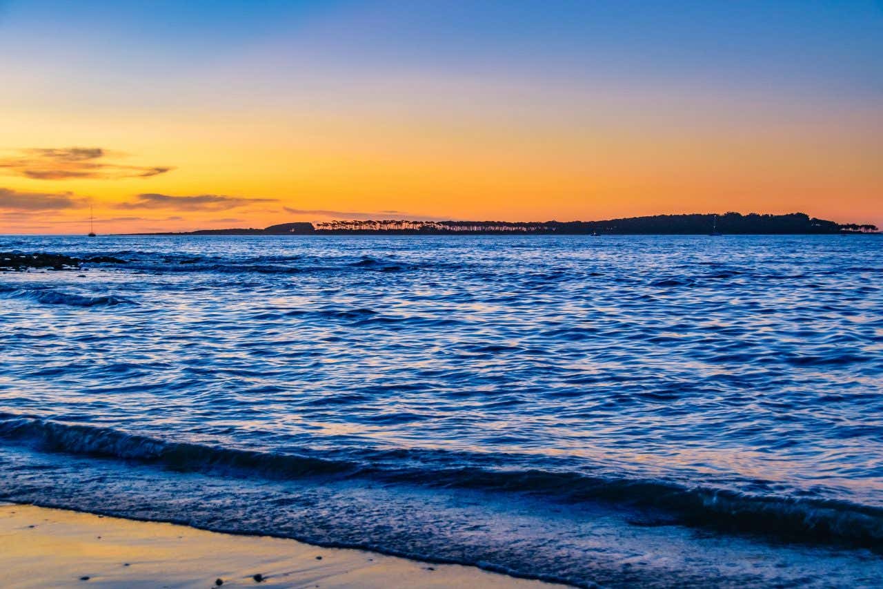 Praia de águas calmas com o céu alaranjado do entardecer