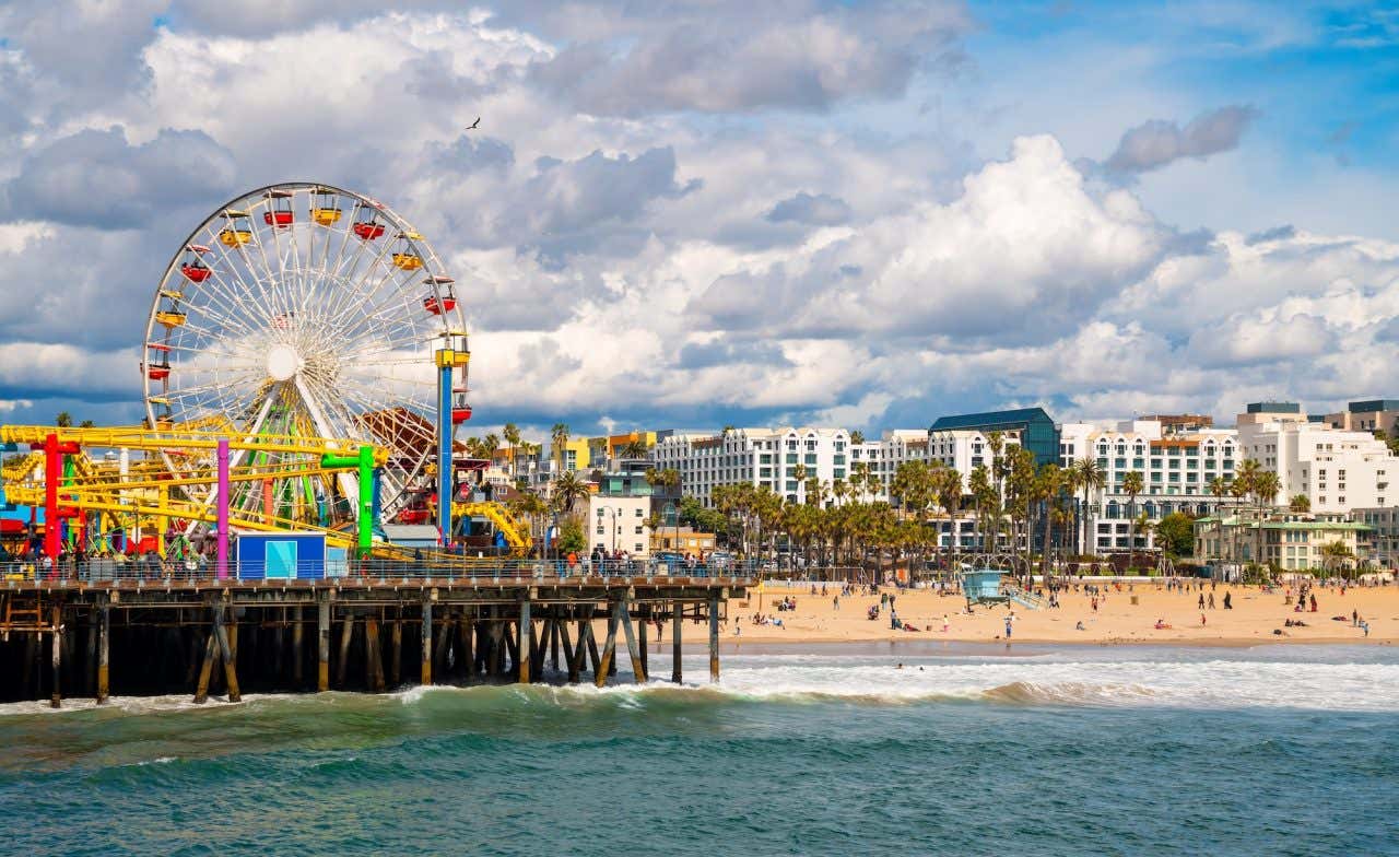 A beach next to a pier with a colorful Ferris wheel viewed from the sea