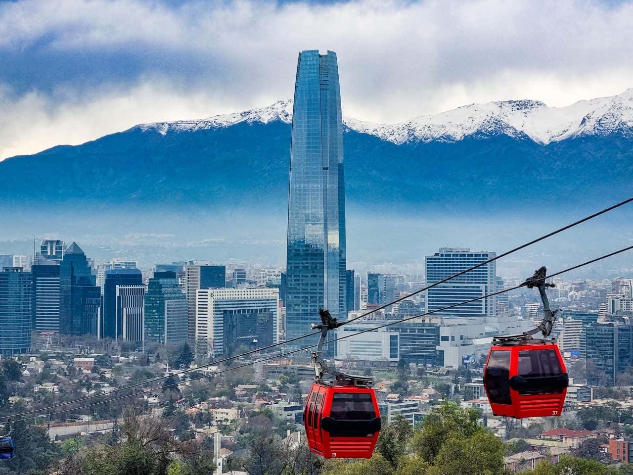 Teleféricos vermelhos passando pela paisagem da cidade de Santiago com a Cordilheira dos Andes ao fundo