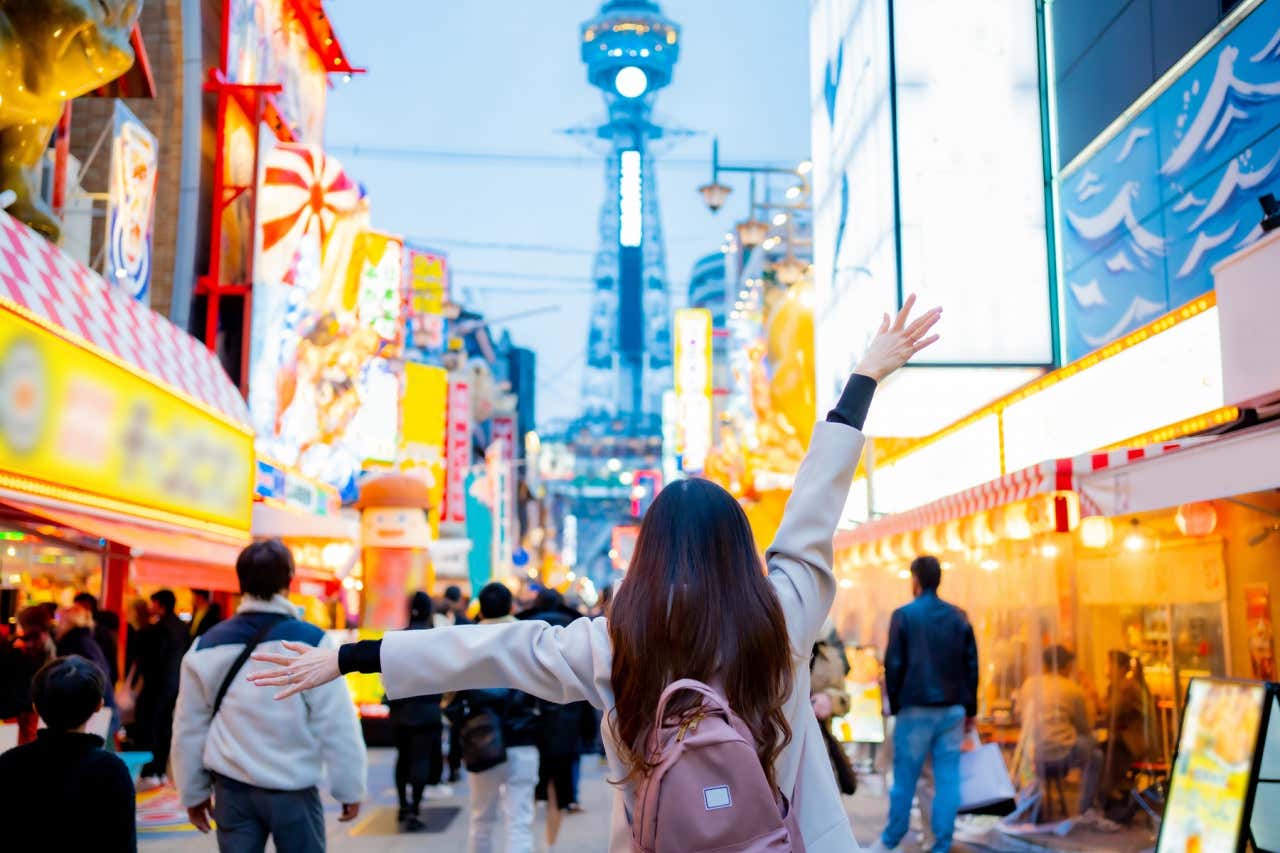 Chica paseando por las calles de Shinsekai al atardecer con las tiendas y edificios iluminados