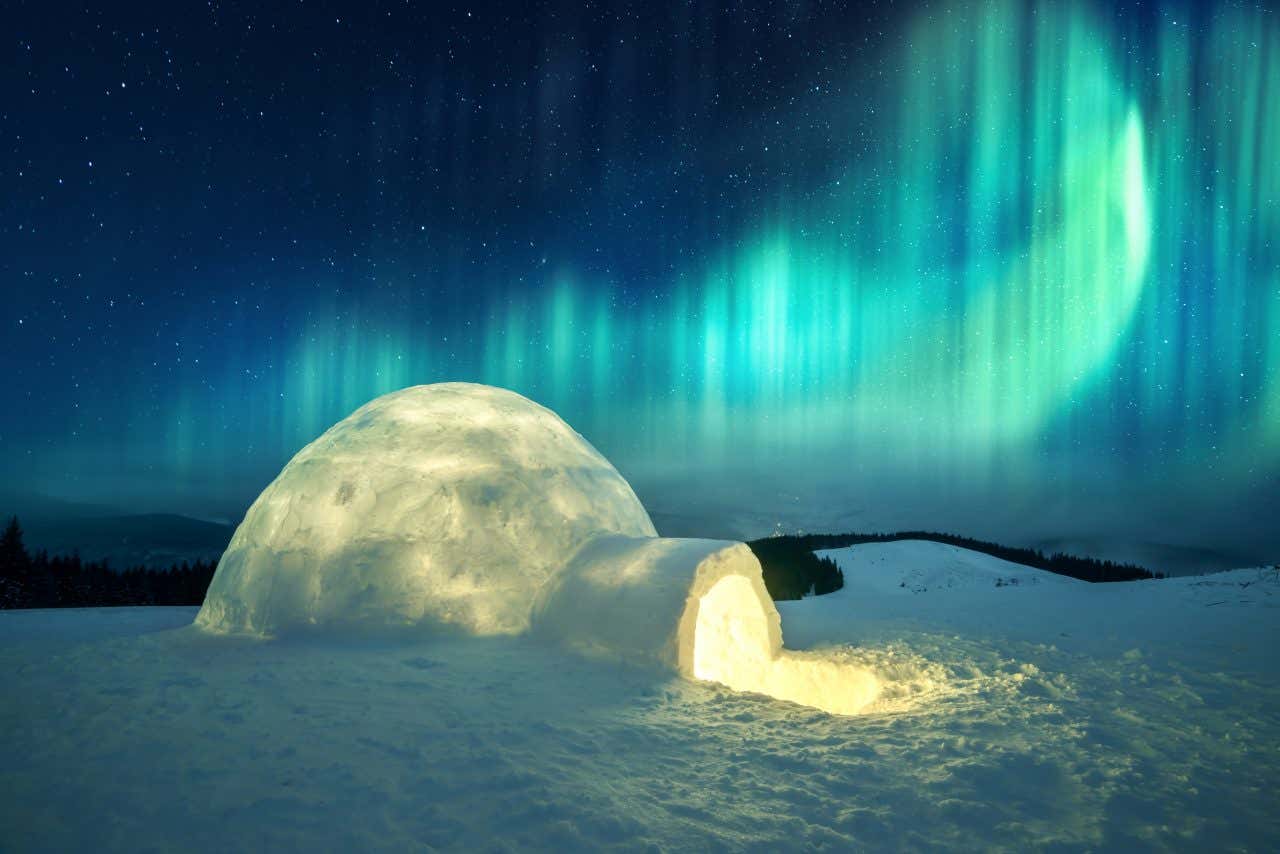 Un igloo illuminé de l'intérieur sous une aurore boréale