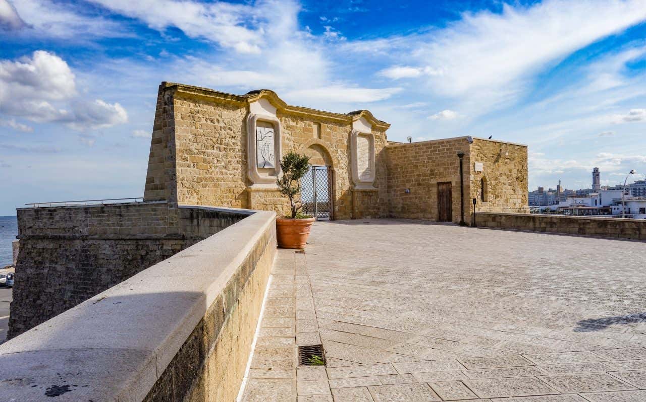 Vista delle mura esterne fortificate di Bari interrotte da un cornicione in pietra con una porta che dà sul mare in un giorno di sole