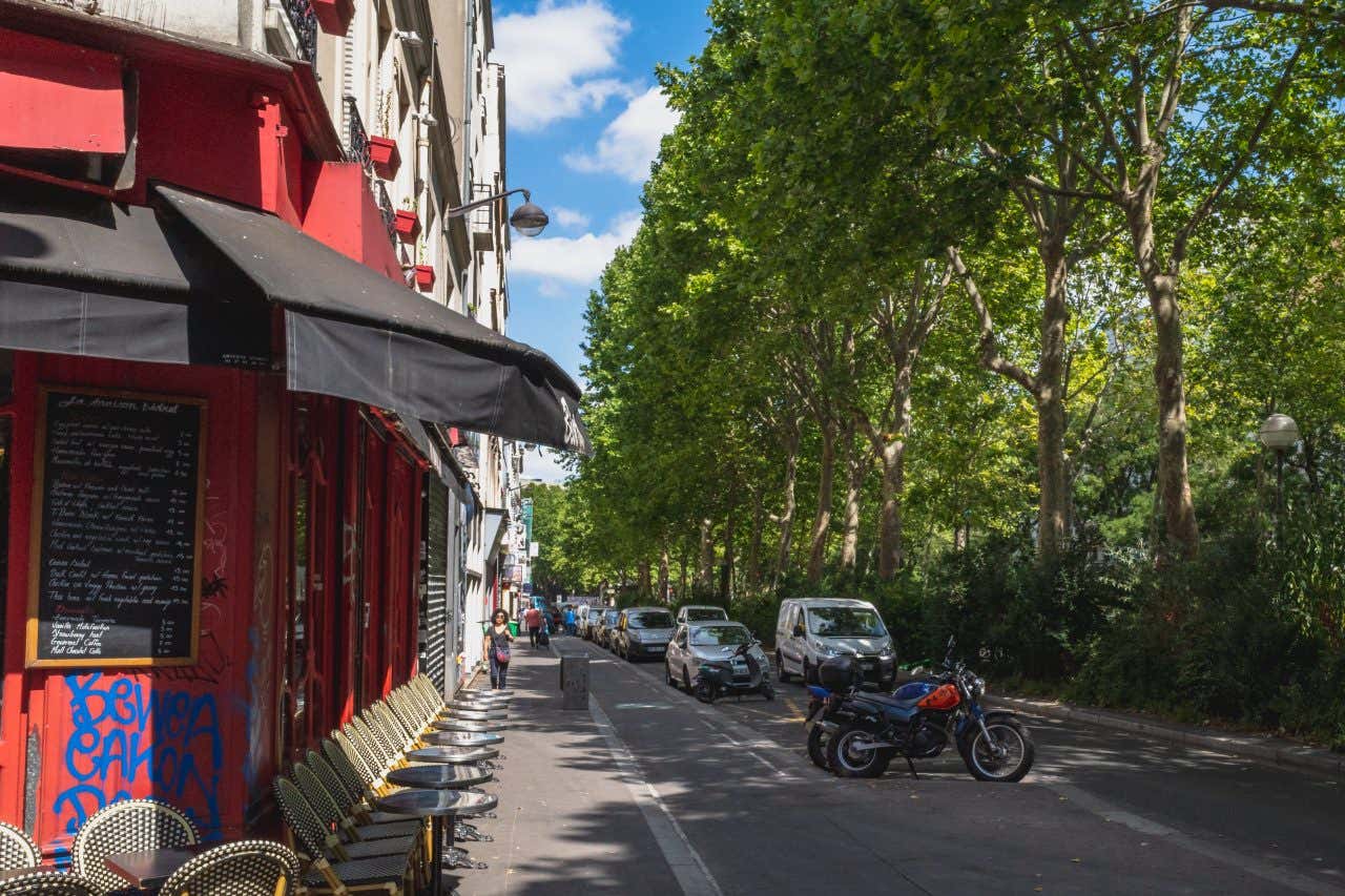 A street in Belleville, with a red shop front on the corner on the left side, and cars and bikes parked along the road beside it.