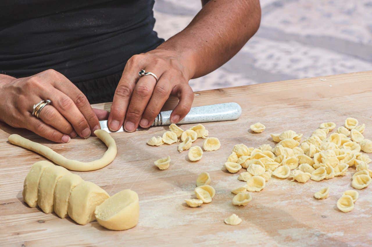 Le mani di una donna che lavorano panetti di pasta fresca per ricavarne delle orecchiette, un tipo di pasta a forma concava