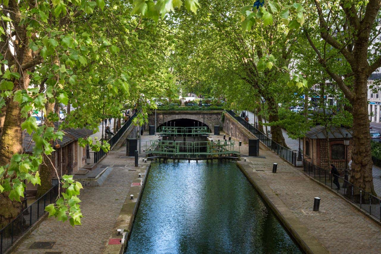 An aerial shot of Canal Saint-Martin, with a bridge visible in the background, and trees lining the walkways on either side.