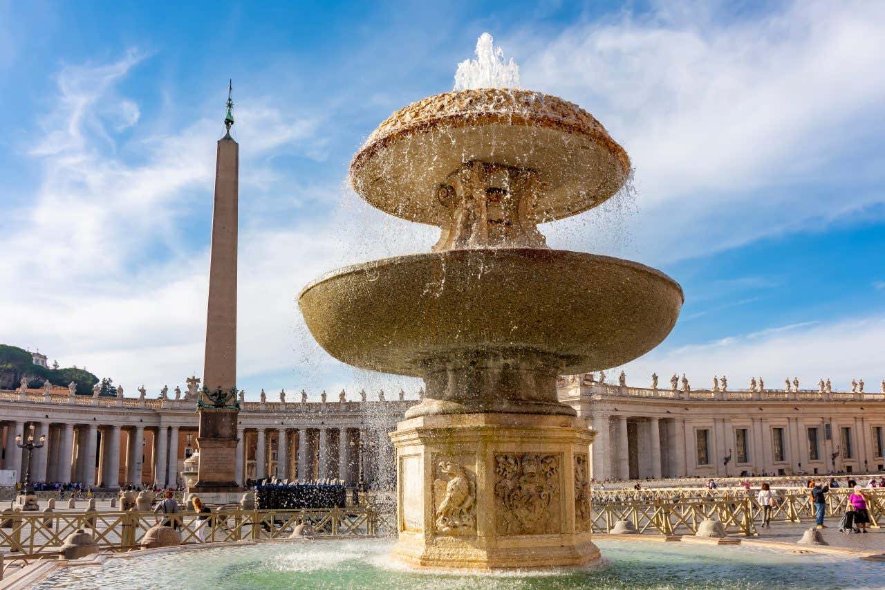 Una grande fontana in primo piano e sullo sfondo un obelisco e i colonnati di piazza San Pietro a Roma in un giorno di sole