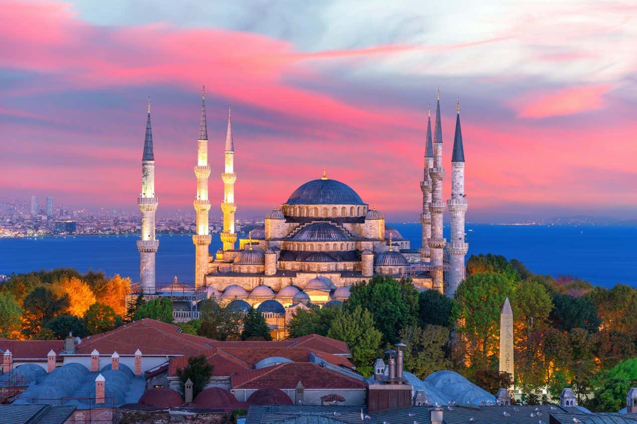 La moschea blu al tramonto illuminata di sera con le sue cupole e le sei torri sottili su ambo i lati, Sullo sfondo il mare e il cielo con sfumature di rosa intenso