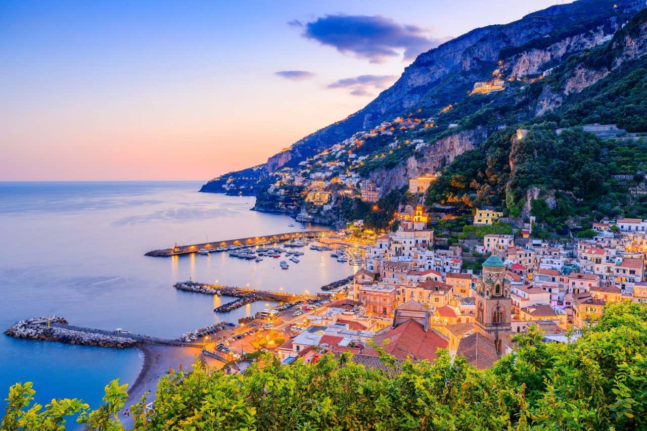 An aerial shot of a hillside on the Amalfi Coast in the evening, with many buildings lit up.