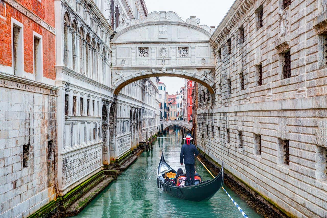 A man wearing a hat sailing along the canals in Venice.