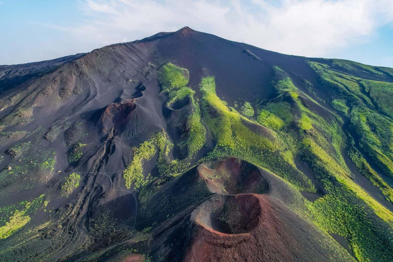 Vista aerea in una giornata di sole della cima del vulcano Etna, con due piccoli crateri attaccati e la punta del monte al vertice