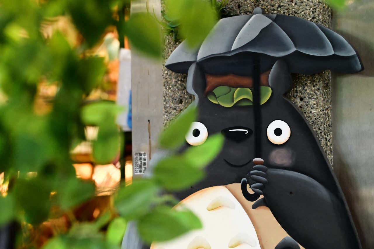 Statue de Totoro avec un parapluie sur un mur, un personnage du Studio Ghibli, une visite incontournabe à faire à Tokyo