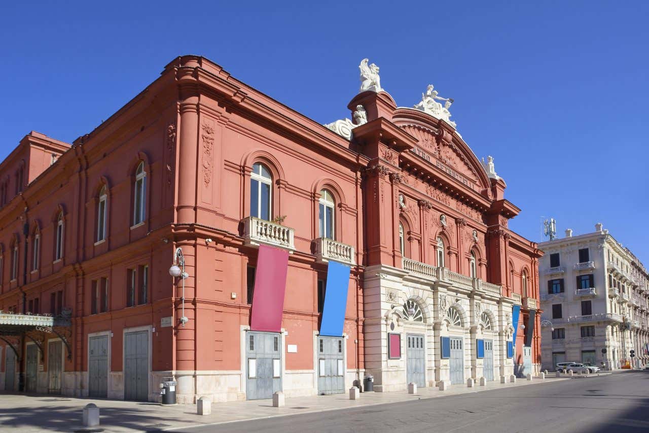 Un edificio in stile liberti di colore arancione e con delle statue bianche che decorano la cima in un giorno di sole senza nuvole