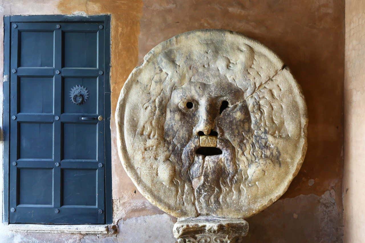 Masque sculpté sur du marbre à côté d'une porte bleue