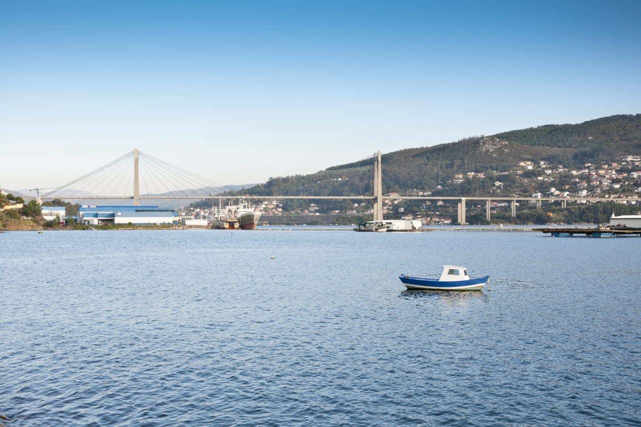 A small boat in the waters of the Ria de Vigowith a bridge and mountain in the background on a sunny day