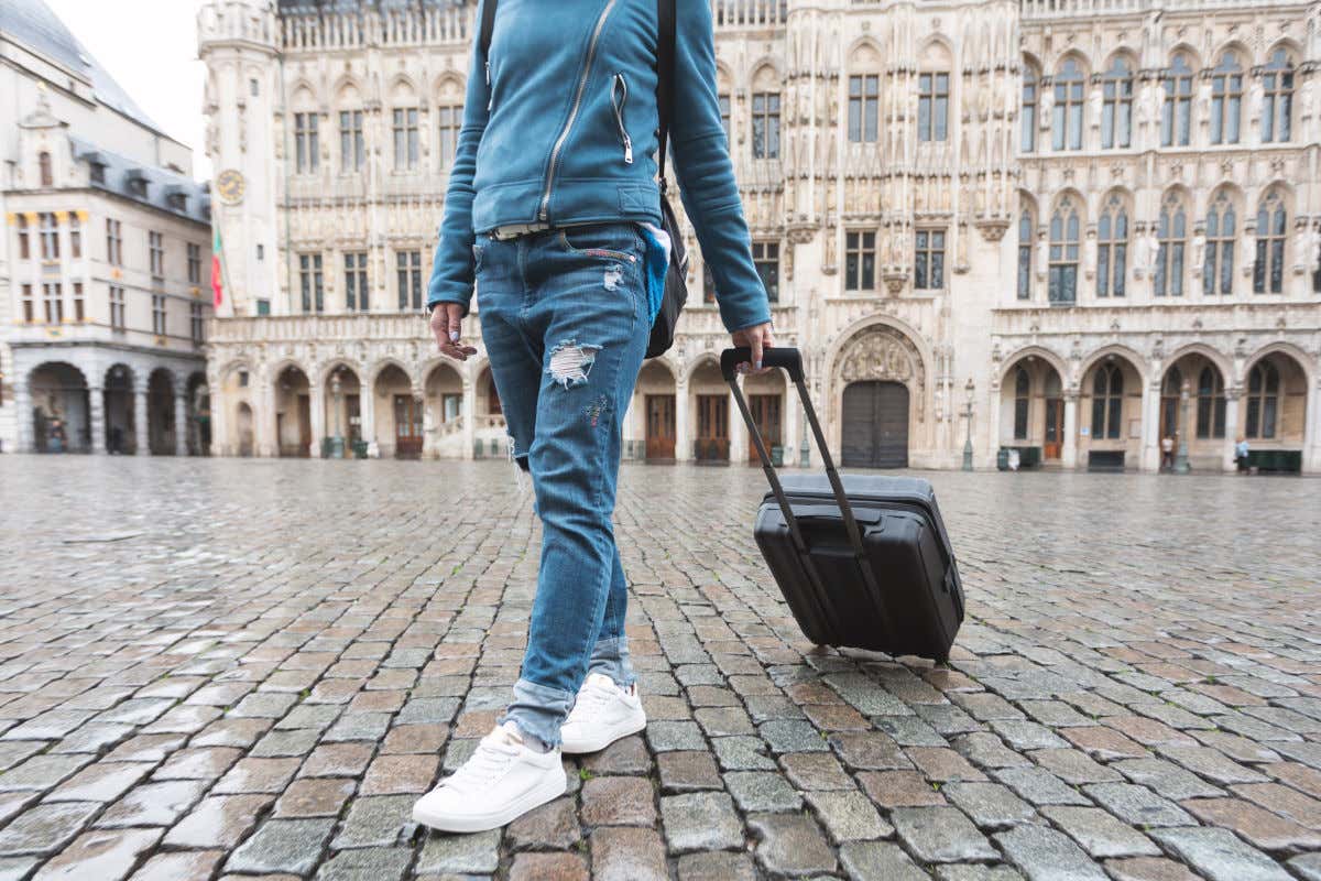 Una turista arrastrando una pequeña maleta por el suelo adoquinado y mojado de la Grand Place de Bruselas