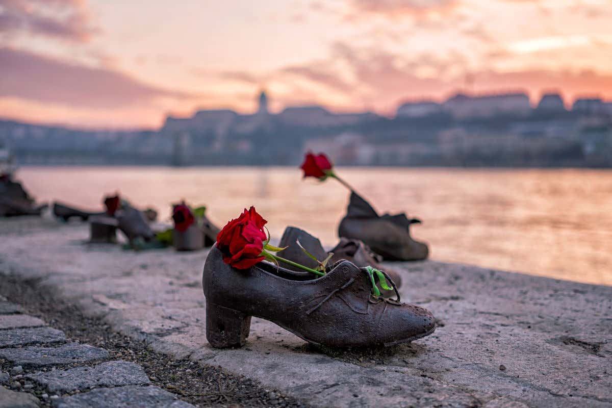 Esculturas de unos zapatos de bronce con flores naturales de color rojo junto a las orillas del río Danubio