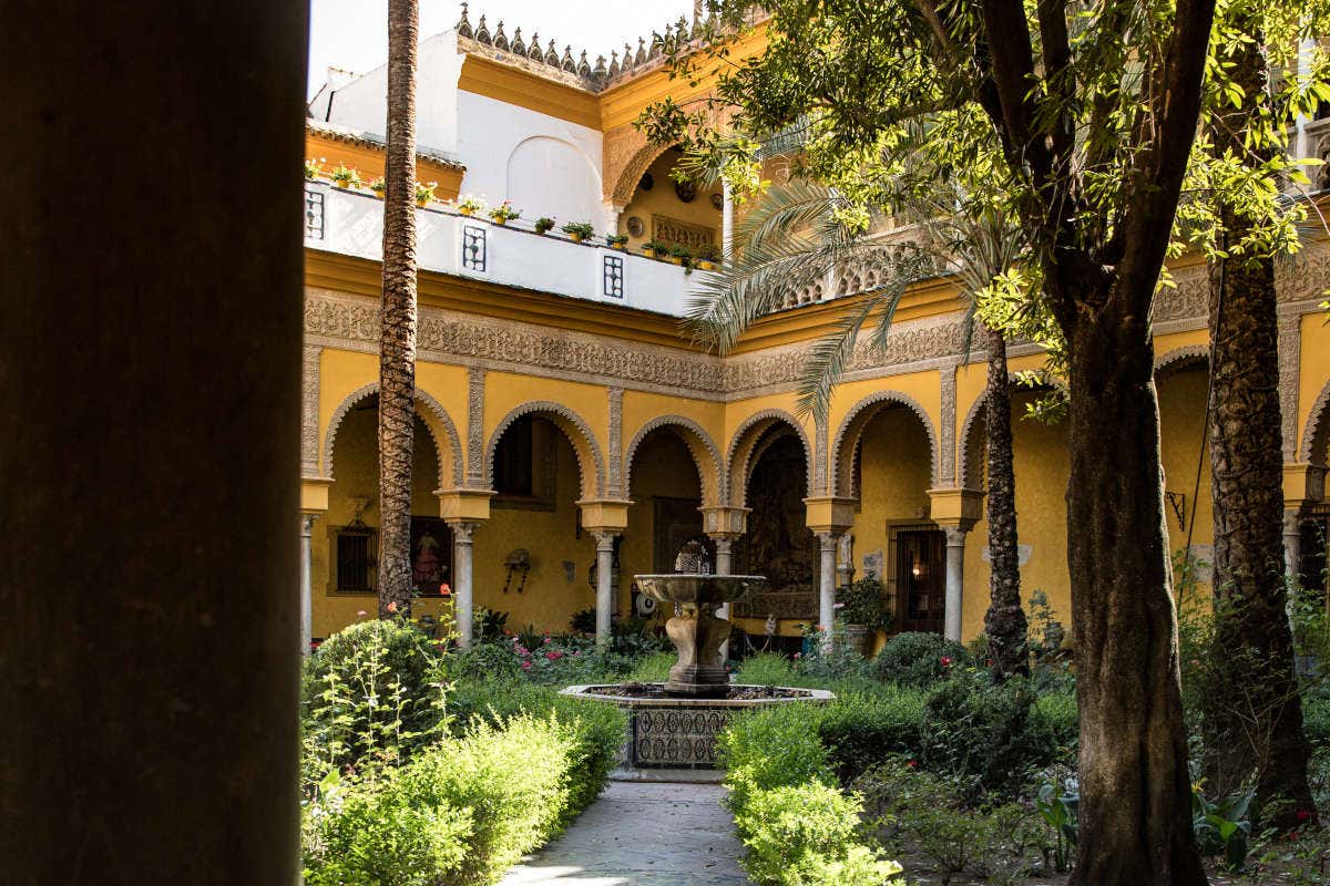 Fuente de piedra en un patio al aire libre del Palacio de las Dueñas con arcos árabes amarillos