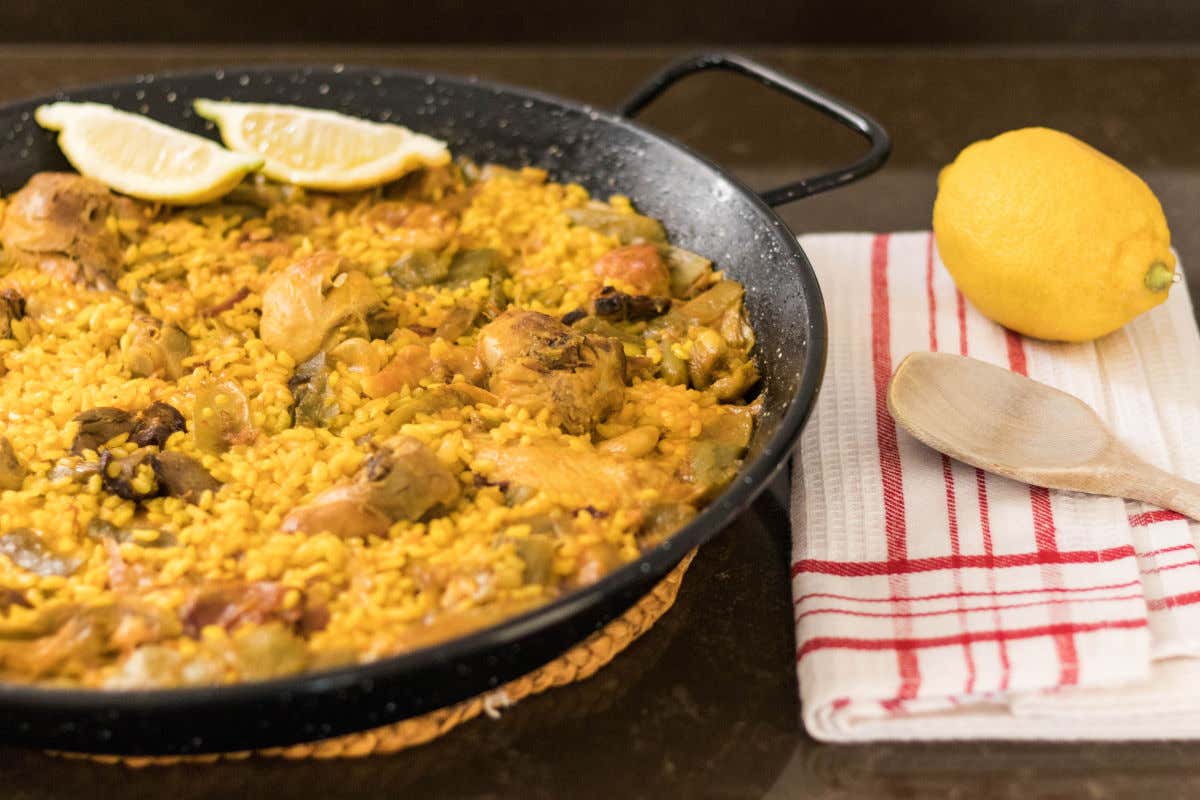 Una paella valenciana con rodajes de limón, conejo y judías verdes