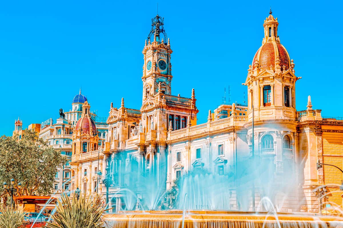 Una fuente en primer plano frente a la fachada del Ayuntamiento de Valencia, que destaca por su torre central con reloj