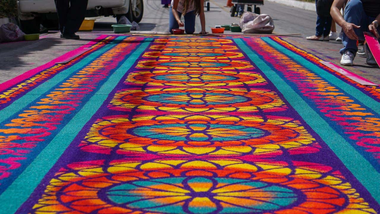 Alcune persone inginocchiate sull'asfalto cospargono petali colorati per creare tappeti colorati decorativi in occasione della Settimana Santa ad Antigua Guatemala