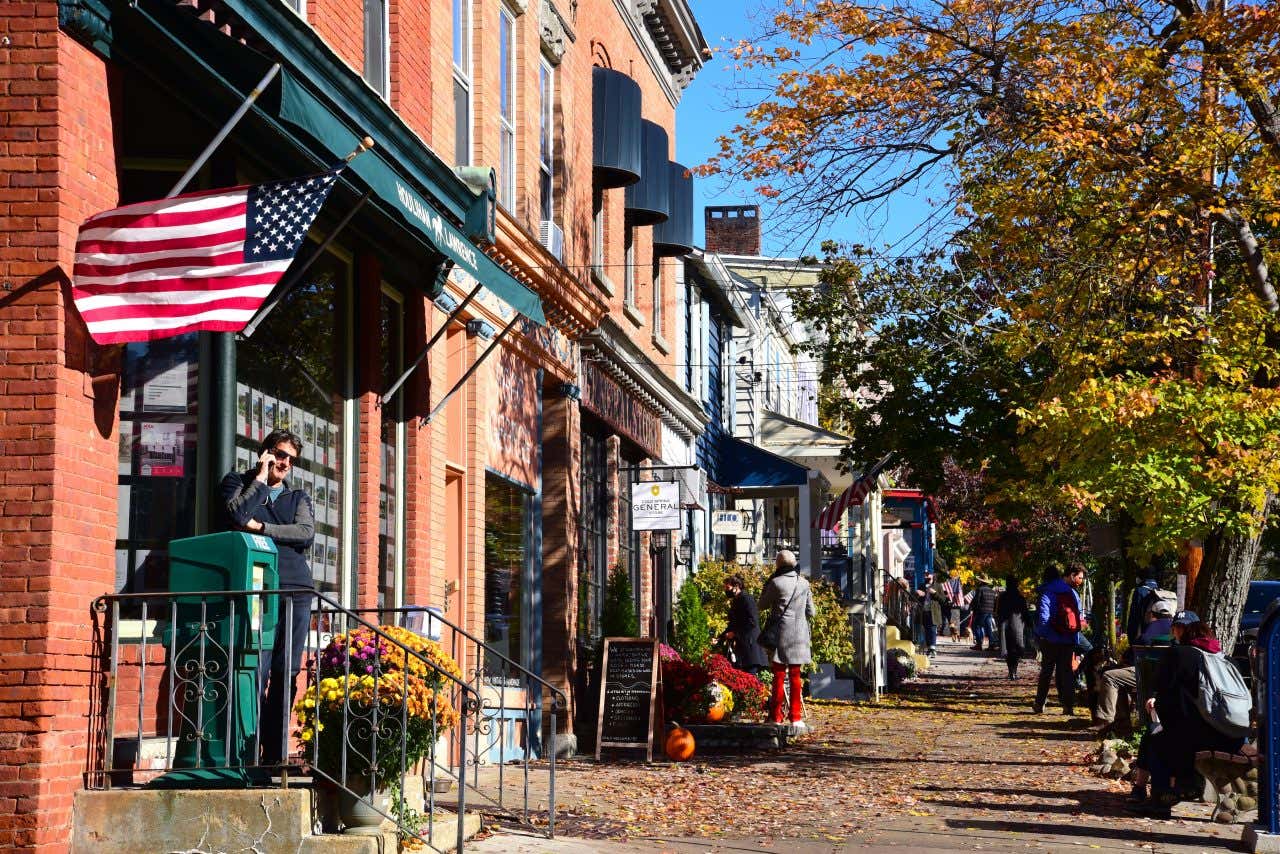 A street in Cold Spring, NY, with an American mounted on a building on the left and shops along the street.