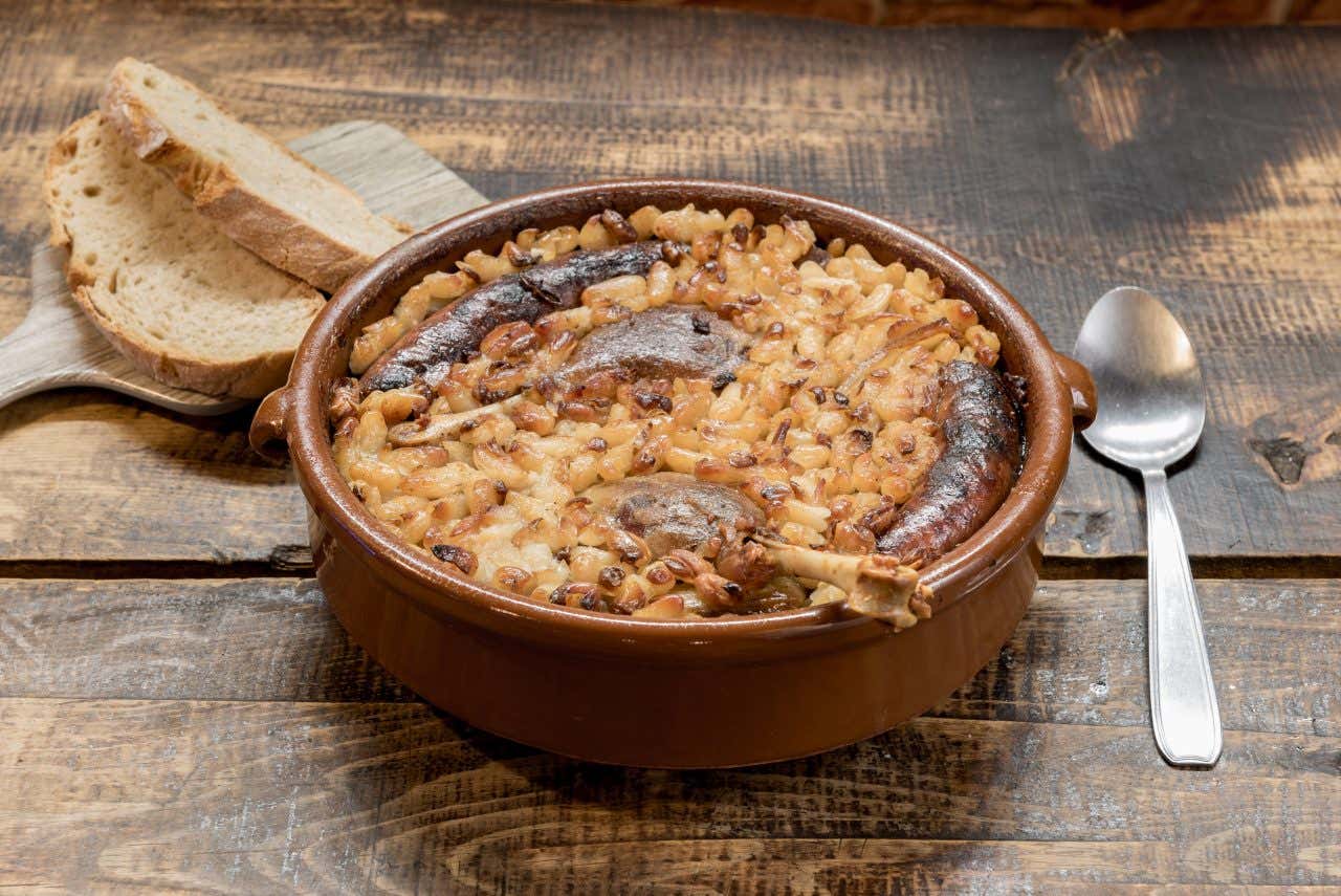 Assiette de cassoulet dans un plat en terre cuite avec du pain et une cuillère