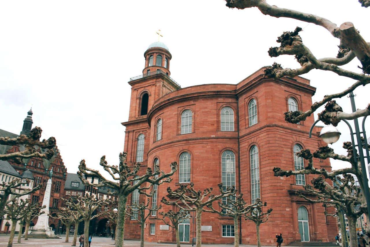 Edifício ovalado de tijolinhos com muitas árvores secas ao redor