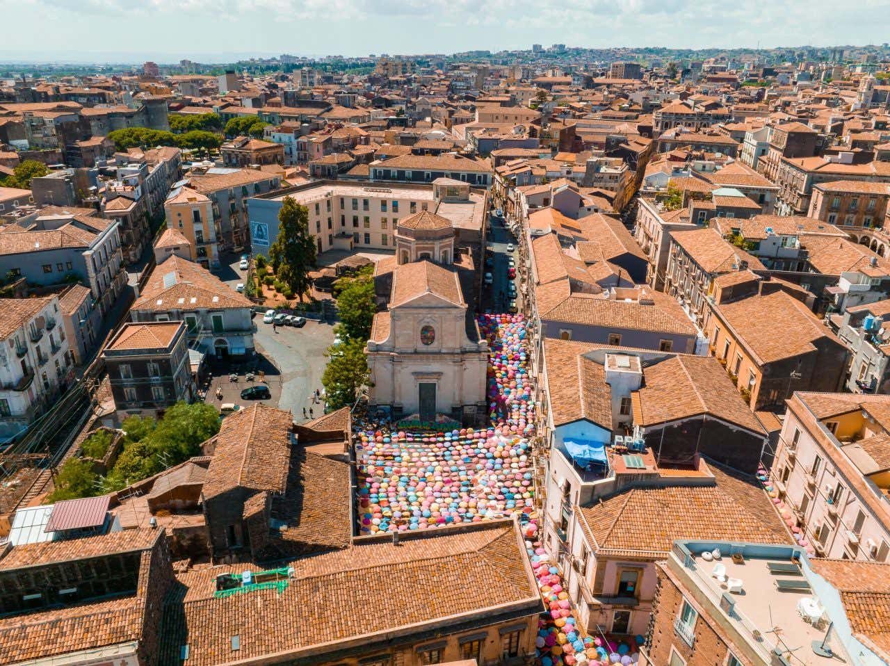 Vista aerea del centro storico di Catania con tanti ombrellini colorati aperti e appesi a coprire una piazza e le vie limitrofe