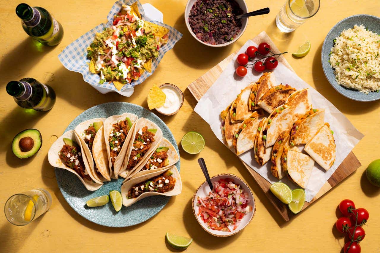 Plusieurs plats avec des tacos, du riz, des légumes sur une table jaune