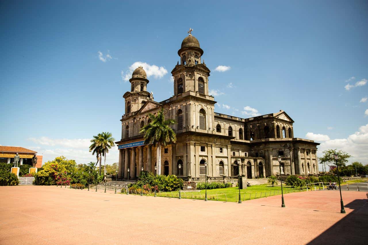 The Old Cathedral of Managua as seen from an angle, with palm trees at its front and a slightly cloudy blue sky in the background.