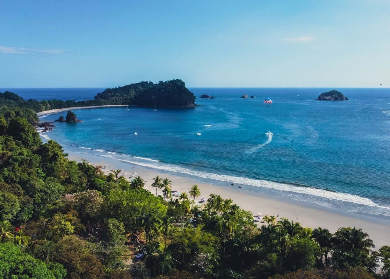 An aerial view of a white sand beach in Manuel Antonio, with deep blue water in the background.