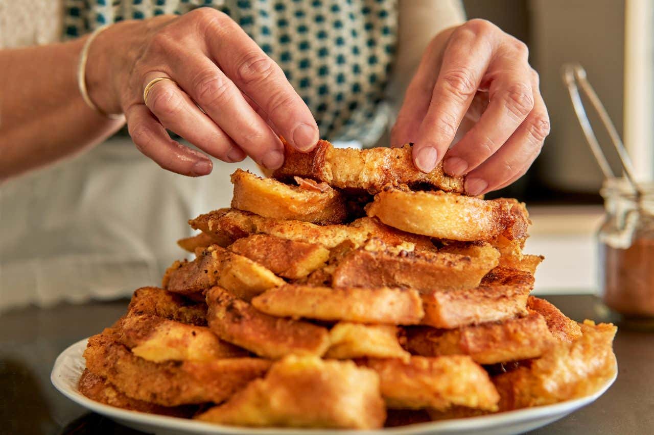 Mani di donna compongono un dolce fatto con fette di pane disposte una sopra l'altra, fritte nell'uovo e condite con miele e cannella