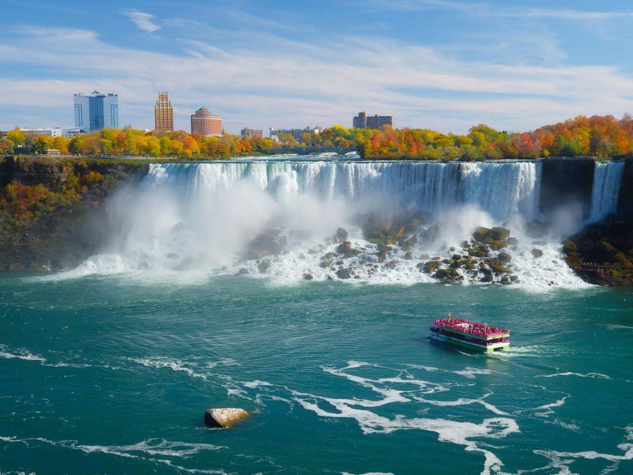 Niagara Falls, New York, with a boat sailing toward the falls, and trees with fall leaves in the background.