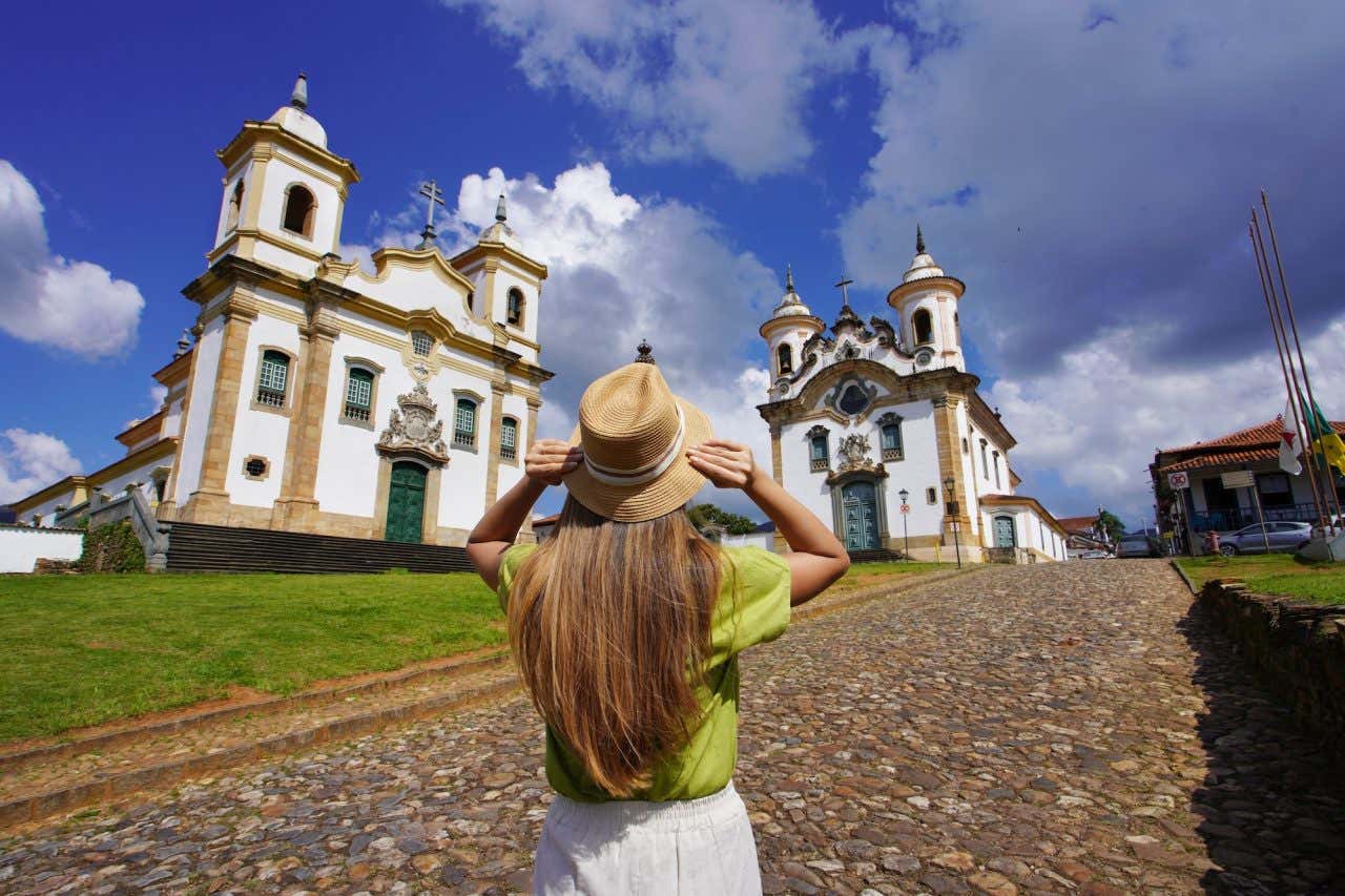 Vista de uma mulher visitando a cidade histórica de Mariana, com duas igrejas de arquitetura colonial barroca