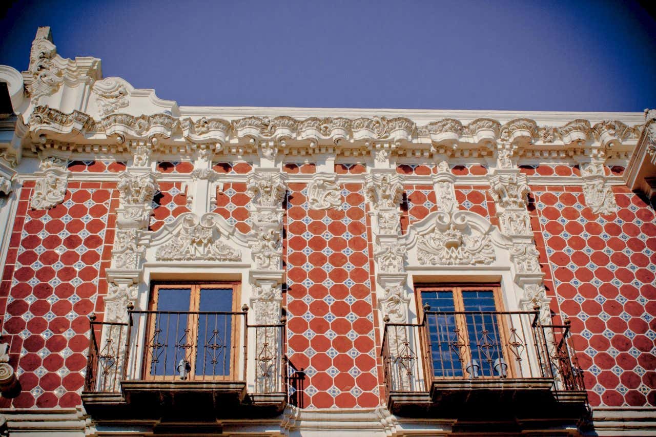 Talavera-tiled building in Puebla, Mexico as seen from the ground, with ornate design around the tiling and a blue sky in the background.