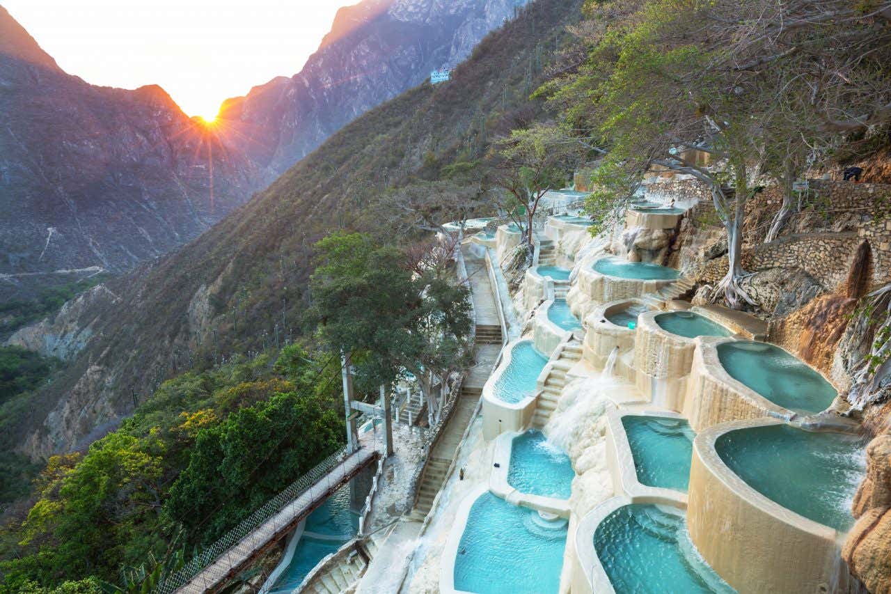 Bright blue pools on a cliffside in Tolantongo, with the sun peaking over the cliffs in the background.