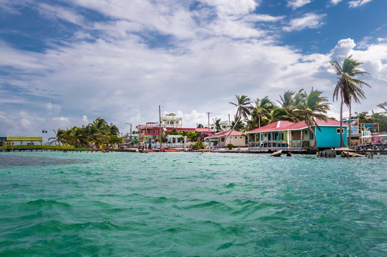 Caye Caulker, Belize as seen from the water with a cloudy blue sky in the background.