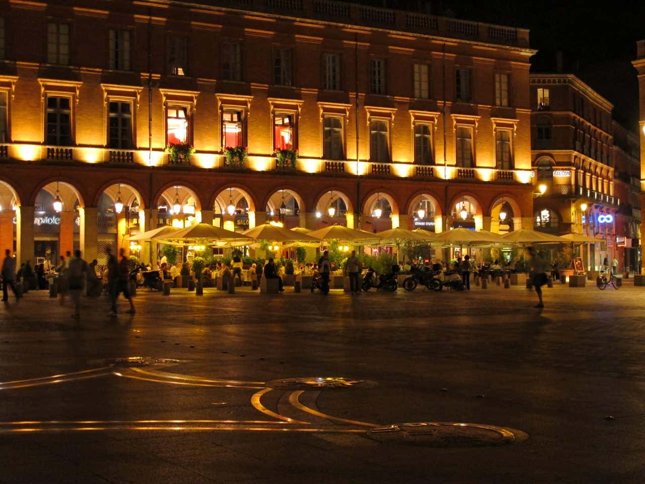 Terrasse d'un restaurant de nuit devant les arches d'un bâtiment illuminé