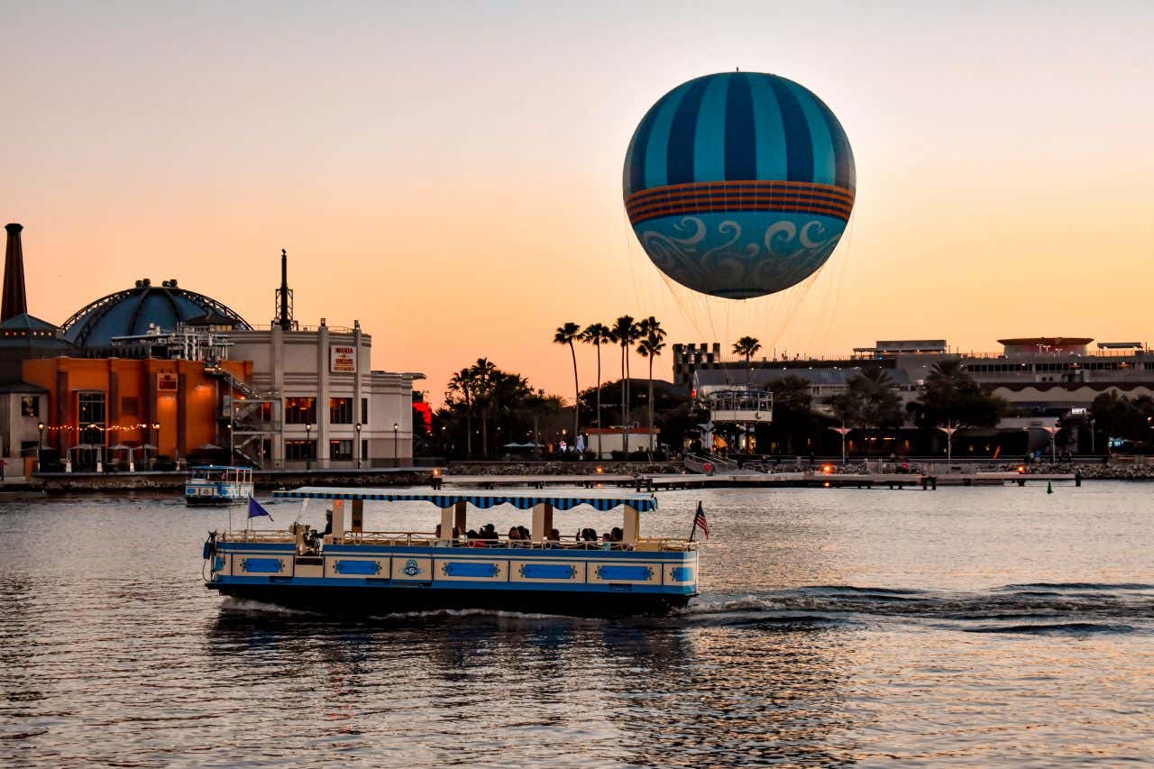 A boat sailing along Walt Disney Orlando with a balloon in the background and an orange sky.
