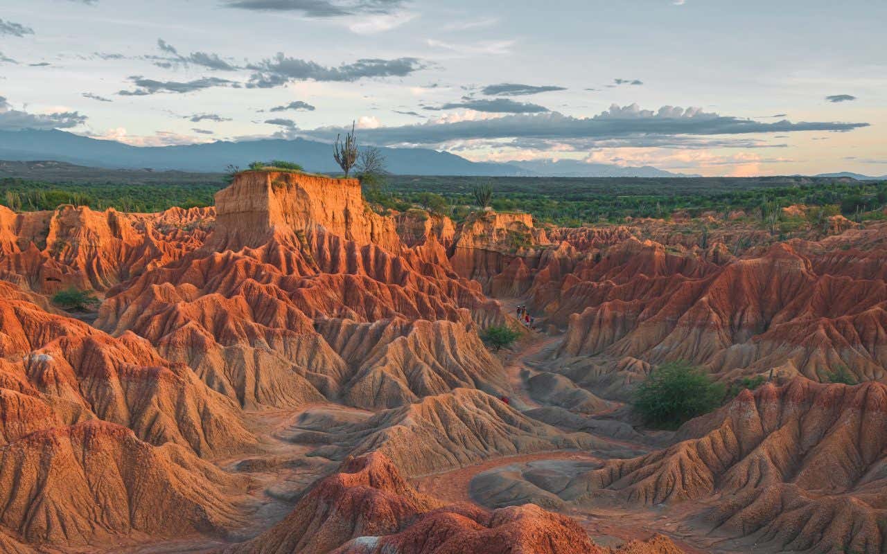 A wide shot of the Tatacoa Desert, Colombia at sunset, with a cloudy grey sky in the background.