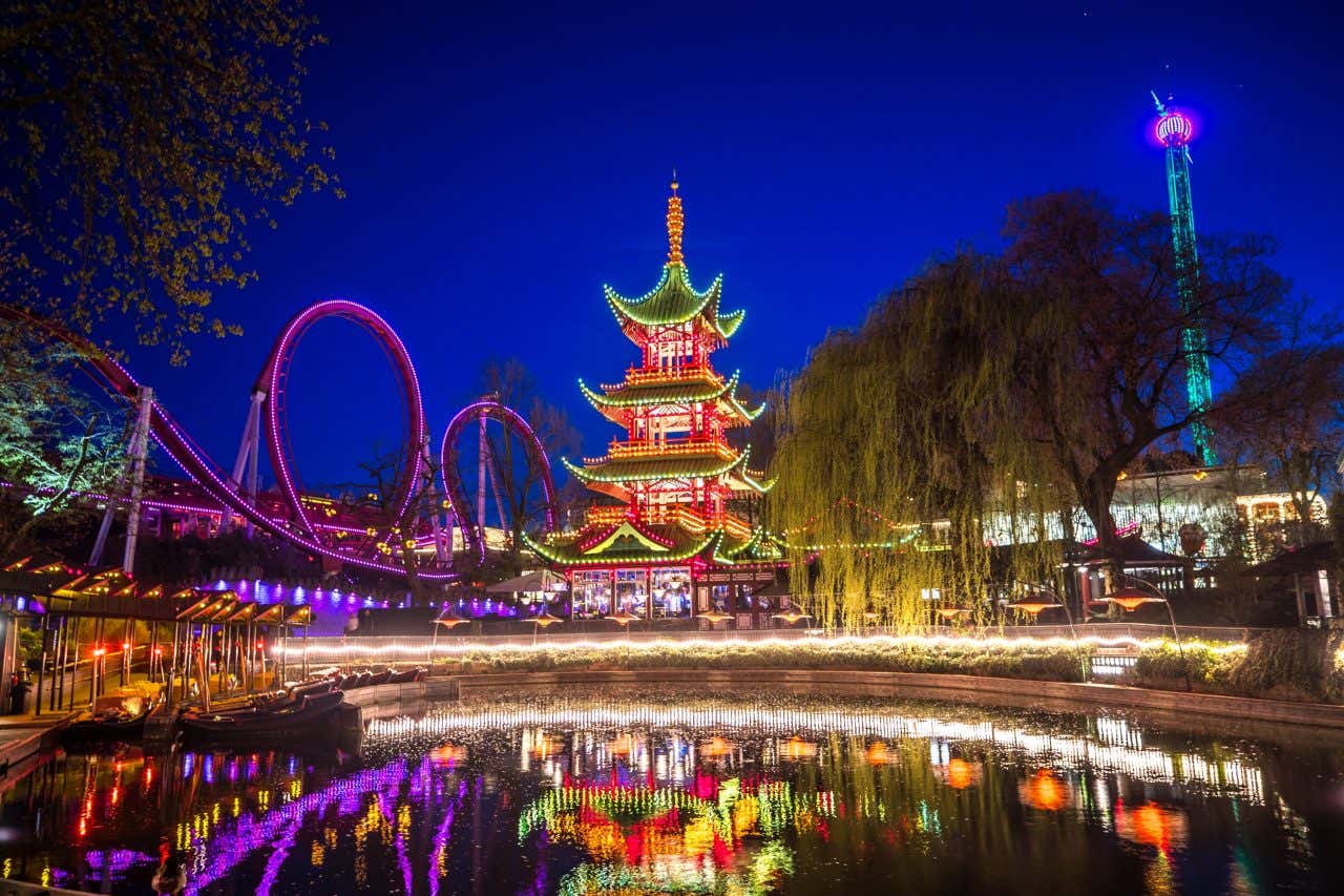 Tivoli Gardens lit up at night, with a Japanese temple and the wooden roller coaster lit up with lights.