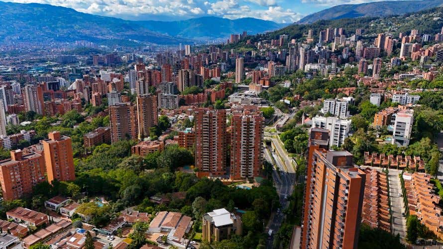 An aerial view of Medellín, Colombia with many high rise apartment blocks in view, and a cloudy sky in the background.